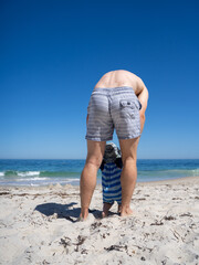Father helping baby learning to walk on a sunny sandy beach