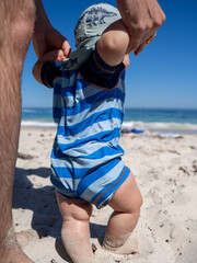 Baby learning to walk on a sunny sandy beach