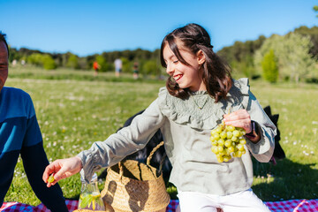 Happy family having fun during a picnic in a park, sharing grapes and drinks, with their dog