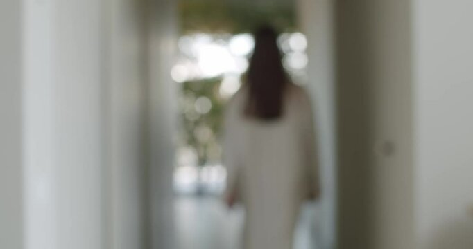 A woman in a white robe walks down a hallway towards a bright, plant-filled room. The video evokes feelings of peace, tranquility, and relaxation, perfect for lifestyle or wellness content.
