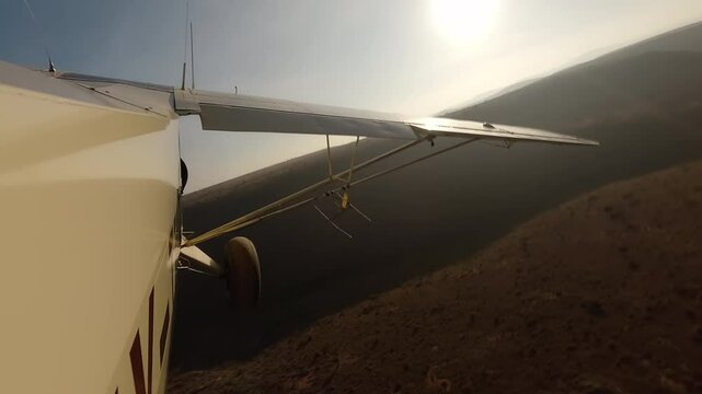 Aerial wide of small air plane side view flying over dry savannah with shrubs and hills in a sunny morning in Kenya
