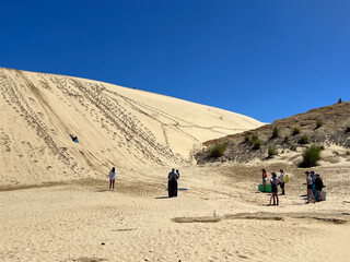 Tourists sand boarding down large sand dunes in Northland New Zealand. Giant Sand Dunes, are a collection of sand dunes located on the Northland Peninsula of New Zealand.