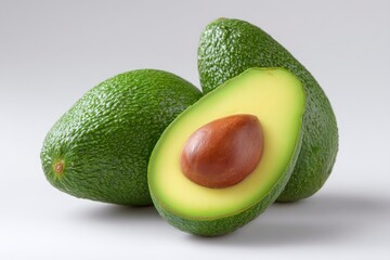 Three avocados on a light background one cut in half with the seed showing