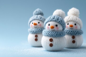 Three knitted snowman figures adorned with hats and scarves stand on a snowdusted surface against a light blue backdrop