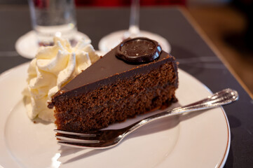 Piece of famous Sachertorte chocolate cake with apricot jam of Austrian origin served with whipped cream in old classic cafe-restaurant in Vienna