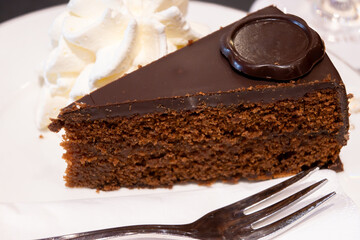 Piece of famous Sachertorte chocolate cake with apricot jam of Austrian origin served with whipped cream in old classic cafe-restaurant in Vienna
