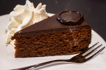 Piece of famous Sachertorte chocolate cake with apricot jam of Austrian origin served with whipped cream in old classic cafe-restaurant in Vienna
