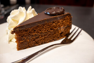 Piece of famous Sachertorte chocolate cake with apricot jam of Austrian origin served with whipped cream in old classic cafe-restaurant in Vienna