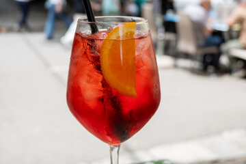 Spritz Campari red bitter long drink cocktail maid with liqueur, prosecco sparkling wine, ice cubes and piece of orange, street view of Palermo, Italy