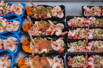 Sea street food for tourists on fish market on promenade in Oostende, Belgium, plastic box with variety of sea shells, shrimps, crab sticks, smoked fish