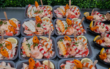 Sea street food for tourists on fish market on promenade in Oostende, Belgium, plastic box with variety of sea shells, shrimps, crab sticks, smoked fish