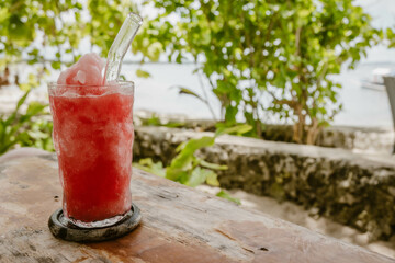Refreshing homemade red coloured slush drink made of watermelon outdoor on a rustic table on the beach at cloud 9 during a summer holiday on Siargao island in the Phillipines in Asia.