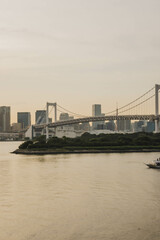 Cityscape of Tokyo skyline with the Rainbow Bridge and boat floating at Tokyo Bay in Odaiba area outdoor at sunset during spring in May in Tokyo city in Japan with space for text.