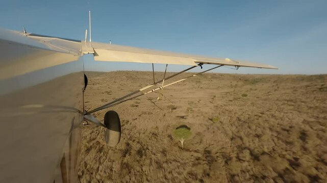 Aerial wide of small air plane side view flying low over dry savannah with shrubs and hills in a sunny morning in Kenya