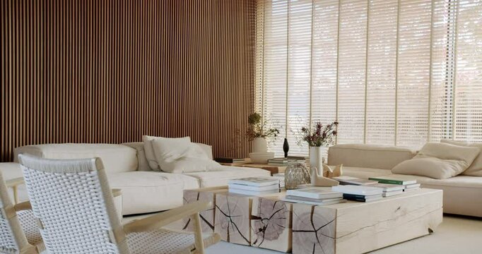 A cozy and stylish living room with wooden furniture, including a unique coffee table, a large couch, and armchairs. Natural light filters through the blinds, creating a warm and inviting atmosphere.
