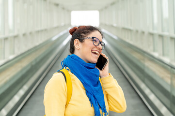 Happy woman stands on a travelator and talks on a cell phone