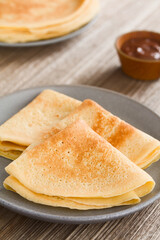 Fresh homemade folded crepes on plate, a pile of crepes and hazelnut or chocolate cream in the back (Selective Focus, Focus one third into the image)