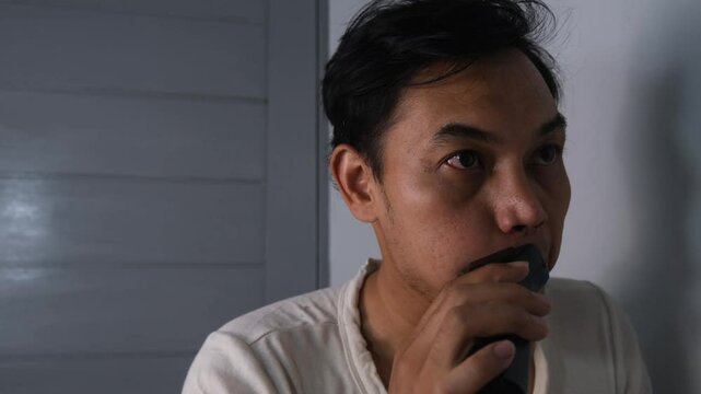 A man wearing a white shirt is shaving his mustache with an electric razor. He focuses on grooming carefully, with the device pressed gently to his upper lip. The scene captures a clean and simple. 4K