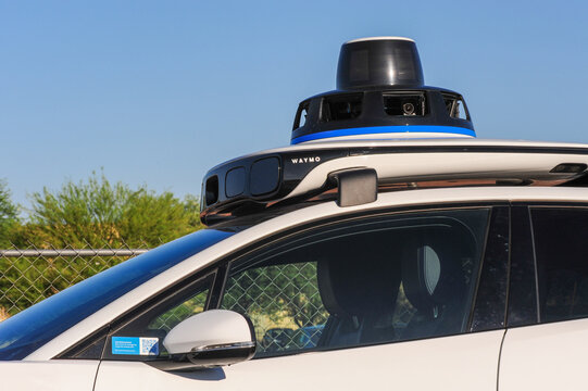 Close-up of Waymo autonomous vehicle with rooftop lidar sensor and external cameras on a white electric Jaguar, showing self-driving technology and advanced mapping systems in urban mobility
