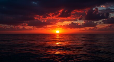 Fototapeta premium A breathtaking ocean sunset paints the sky and water in fiery shades of red and orange. Dramatic clouds add intensity to