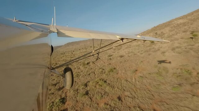 Aerial wide of small air plane side view flying over dry savannah with shrubs, road and hills in a sunny morning in Kenya