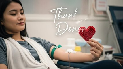 A calm and confident woman donates blood while holding a red heart-shaped symbol. 4K footage video - Powered by Adobe