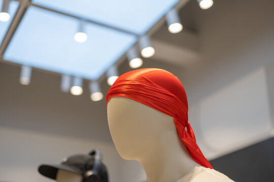 Minimalist mannequin head wearing a bright red durag under spotlight, displayed in a modern retail store with a geometric ceiling and stylish ambiance.