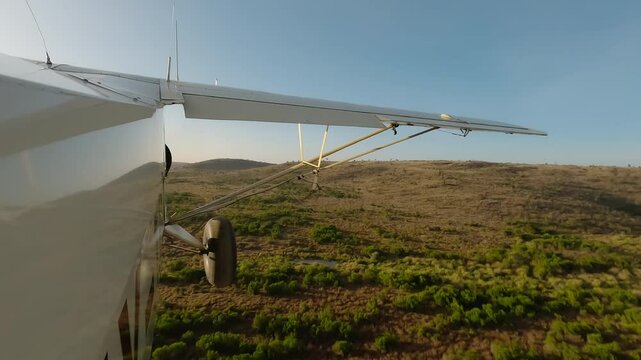 Aerial wide of small air plane side view flying over dry grassy savannah with shrubs and hills in a sunny morning in Kenya