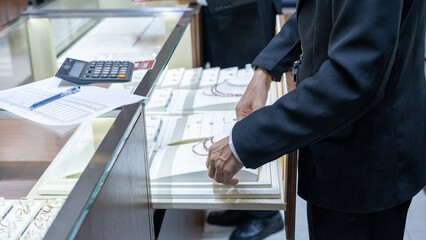 Close-up of a jewelry store clerk arranging gold necklaces in a showcase, with a calculator and...