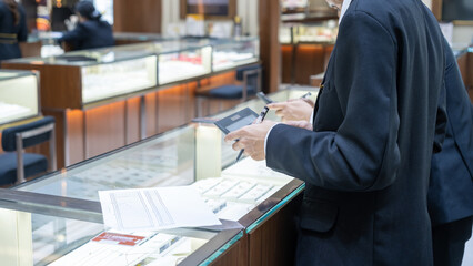 Close-up of jewelry store staff in suits using calculators and checking documents on a glass...