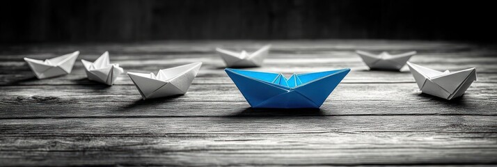 A blue origami paper boat surrounded by multiple white origami boats on a textured wooden surface symbolizing leadership and standing out