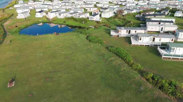 Rows of white holiday cottages with small ponds on green coastal land, Sheringham