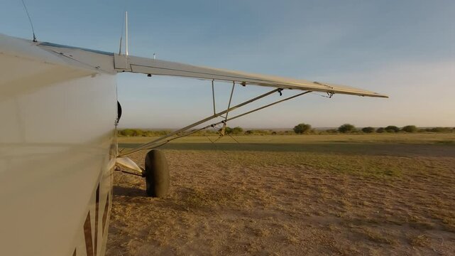 Wide of small air plane side view starting engine next to runway and moving forward in savannah in a sunny morning in Kenya