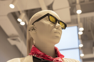Close-up of a stylish mannequin wearing yellow sunglasses and red bandana scarf under store...