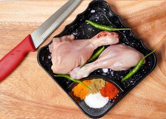 Raw chicken drumsticks with seasonings and green chilies on wooden cutting board background....
