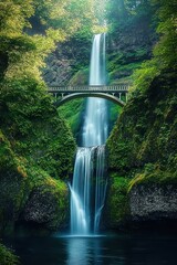 Twin-tiered waterfall cascading between lush green cliffs with arched pedestrian bridge spanning mid-height, surrounded by dense vibrant forest foliage