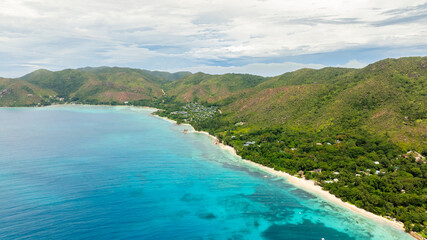 Aerial view of lush green hills descending to turquoise waters and sandy shores, creating a serene...
