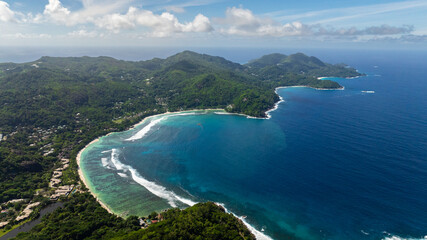 Obraz premium Clear turquoise waters flowing into a white sandy bay surrounded by lush greenery. Seychelles, Mahe.