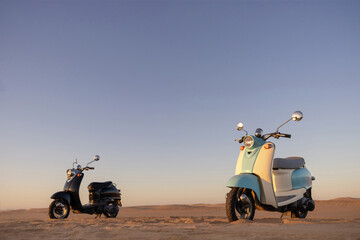 Retro scooters in the Namib Desert glow in soft sunset light, evoking a sense of adventure, escape,...