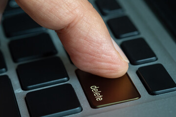 Finger of the computer user, he presses the delete button on the computer keyboard.	
