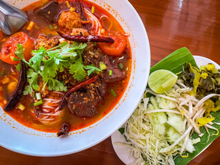 Traditional Thai noodle soup called “Nam Ngiao” served with fresh vegetables on the side. This Northern Thai dish features rice noodles in a spicy and tangy tomato-based broth with pork, dried chili