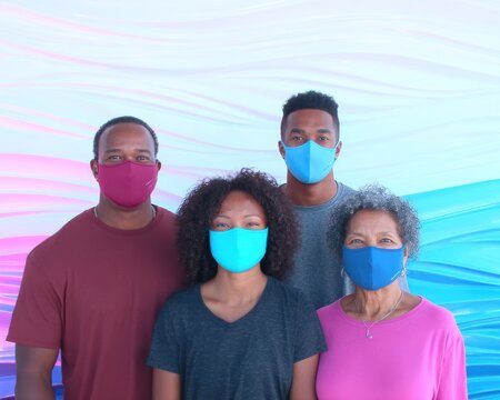 A family of four wearing face masks, smiles and poses in front of a colorful background - Powered by Adobe