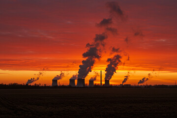 Naklejka premium Industrial power plant emitting smoke against colorful sunset sky 