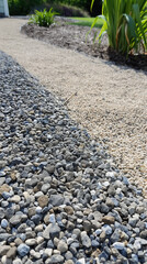Gravel pathway with curving design and green foliage in sunlit garden landscape