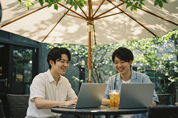 Portrait of two Young Asian enjoying drink together while working on laptop at outdoor cafe, representing remote work flexibility, entrepreneurship, and digital nomad lifestyle