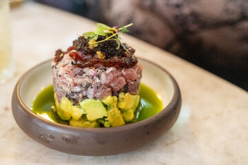 A beautifully plated tartare featuring fresh fish layered with creamy avocado. The dish is garnished with toppings and presented in a stylish bowl, showcasing vibrant colors and textures.