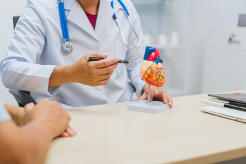 Asian male doctor specializing in cardiology explains heart disease to a patient using a heart...