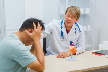 Asian male doctor specializing in cardiology explains heart disease to a patient using a heart...