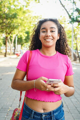 Young latin woman using mobile phone walking in a park