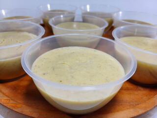 A collection of individual servings of banana pudding in clear plastic cups, arranged on a wooden surface. Represents desserts, catering, comfort food, individual portions, or sweet treats